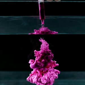 Pink ink dispersing in water from a syringe, creating abstract patterns and vivid textures.